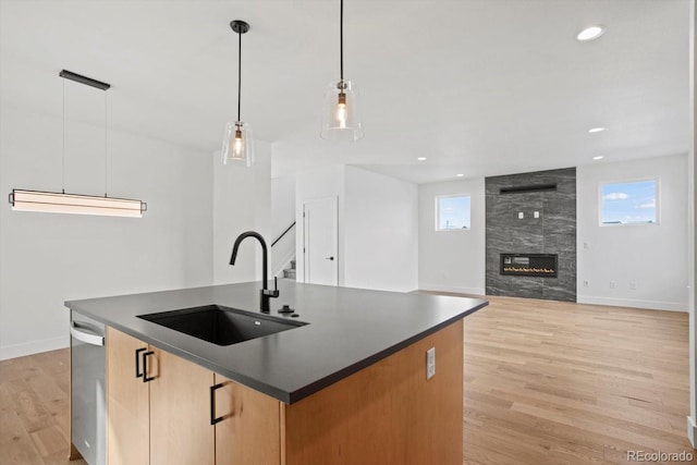 kitchen with sink, a center island with sink, a tiled fireplace, decorative light fixtures, and light wood-type flooring