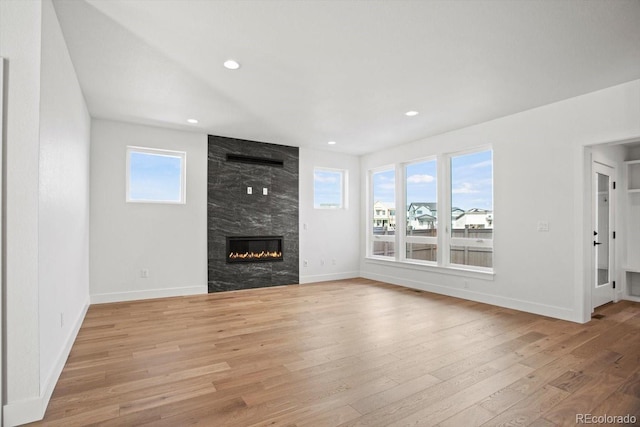 unfurnished living room featuring a high end fireplace, light hardwood / wood-style flooring, and a wealth of natural light