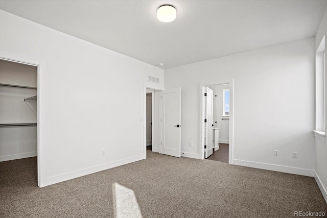 unfurnished bedroom featuring a closet, a walk in closet, dark carpet, and ensuite bath