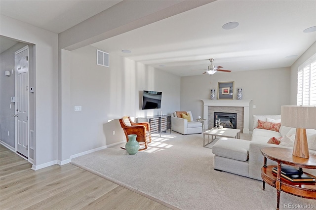 living room with a stone fireplace, light hardwood / wood-style flooring, and ceiling fan