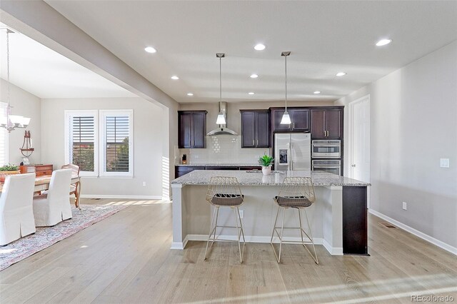 kitchen featuring wall chimney exhaust hood, stainless steel appliances, light stone counters, and a kitchen island