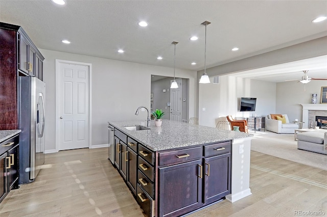 kitchen featuring a center island with sink, decorative light fixtures, appliances with stainless steel finishes, light stone counters, and a fireplace