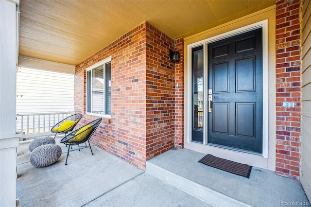 doorway to property featuring covered porch and brick siding