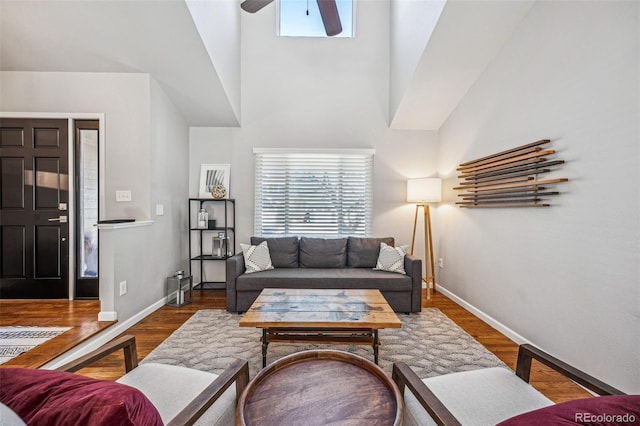 living area featuring ceiling fan, wood finished floors, a towering ceiling, and baseboards