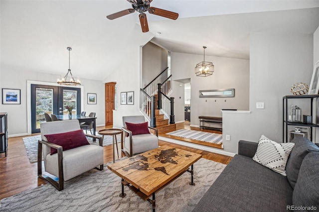 living room featuring high vaulted ceiling, ceiling fan with notable chandelier, wood finished floors, baseboards, and stairs