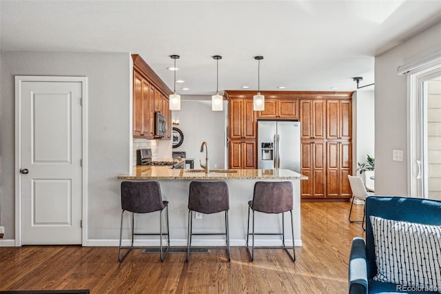 kitchen featuring a breakfast bar, stainless steel appliances, light wood-style flooring, brown cabinetry, and a peninsula