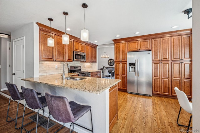 kitchen with stainless steel appliances, a peninsula, light wood-style floors, light stone countertops, and brown cabinetry