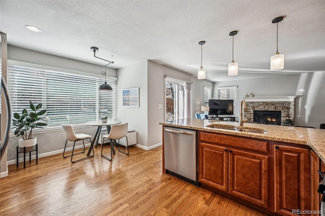 kitchen with light stone counters, light wood-style flooring, a sink, appliances with stainless steel finishes, and pendant lighting