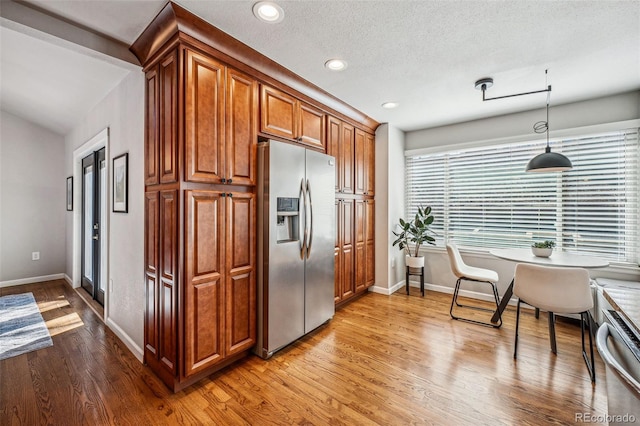 kitchen featuring a textured ceiling, light wood-style flooring, stainless steel appliances, hanging light fixtures, and brown cabinets