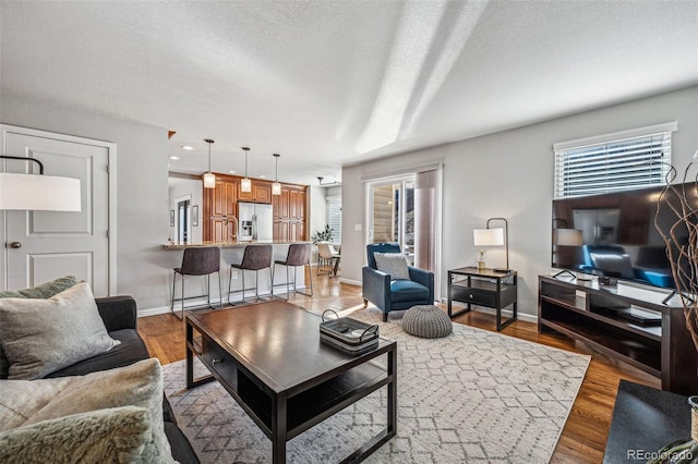 living room featuring a textured ceiling, baseboards, and light wood-style floors