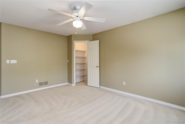 unfurnished bedroom with light carpet, a closet, ceiling fan, and a walk in closet