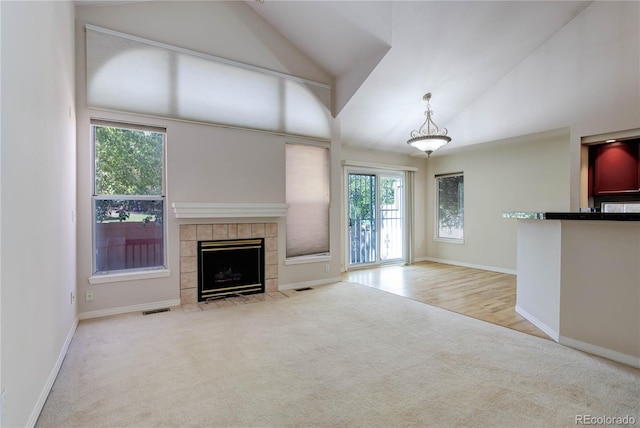 unfurnished living room with light carpet, a tiled fireplace, and high vaulted ceiling