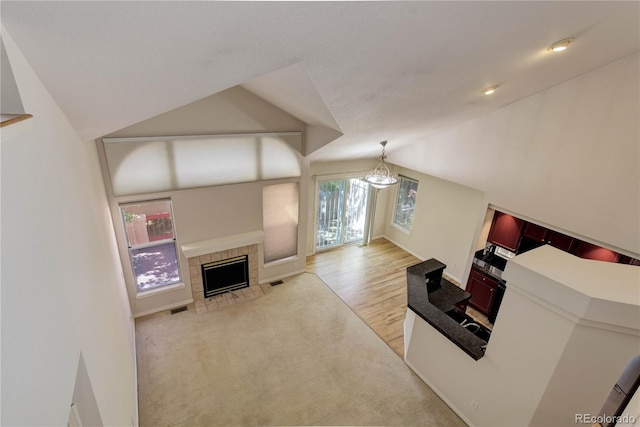 living room with light hardwood / wood-style floors, lofted ceiling, a tiled fireplace, and plenty of natural light