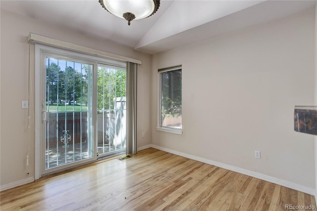 spare room featuring a healthy amount of sunlight, vaulted ceiling, and light hardwood / wood-style flooring