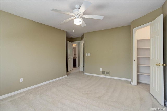 unfurnished bedroom featuring light carpet, ceiling fan, a walk in closet, and a closet