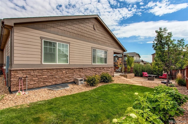 rear view of house with a lawn, an outdoor fire pit, a patio area, fence, and stone siding