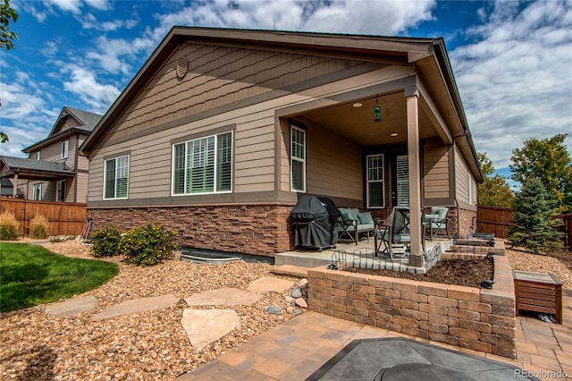 back of property with stone siding, fence, and a patio