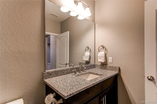 bathroom featuring a textured wall, vanity, visible vents, and an inviting chandelier