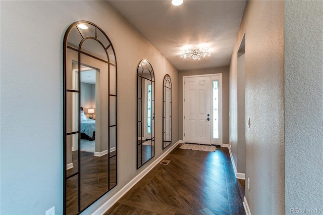 entryway with dark wood-style flooring, visible vents, a textured wall, and baseboards