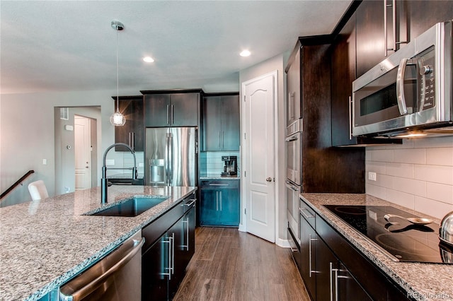 kitchen with light stone counters, stainless steel appliances, dark wood-type flooring, a sink, and hanging light fixtures