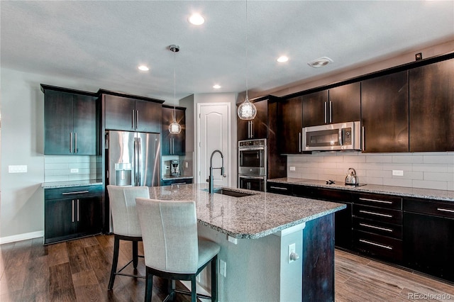 kitchen with dark wood-style floors, appliances with stainless steel finishes, a sink, and light stone countertops