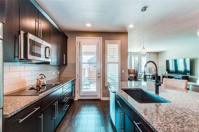 kitchen with tasteful backsplash, dark wood-style floors, stainless steel appliances, pendant lighting, and a sink