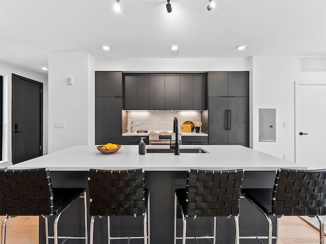 kitchen featuring a spacious island, a sink, light countertops, backsplash, and electric panel