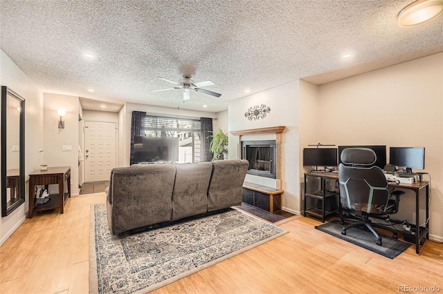 living area with a fireplace, ceiling fan, a textured ceiling, wood finished floors, and baseboards