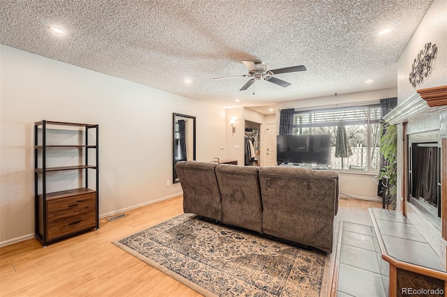 living area with light wood finished floors, ceiling fan, a textured ceiling, a tile fireplace, and baseboards