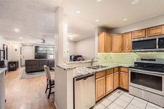 kitchen featuring open floor plan, a sink, light stone countertops, stainless steel appliances, and backsplash