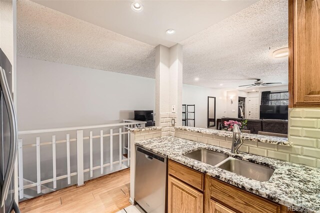 kitchen with a ceiling fan, dishwasher, light stone countertops, light wood-type flooring, and a sink