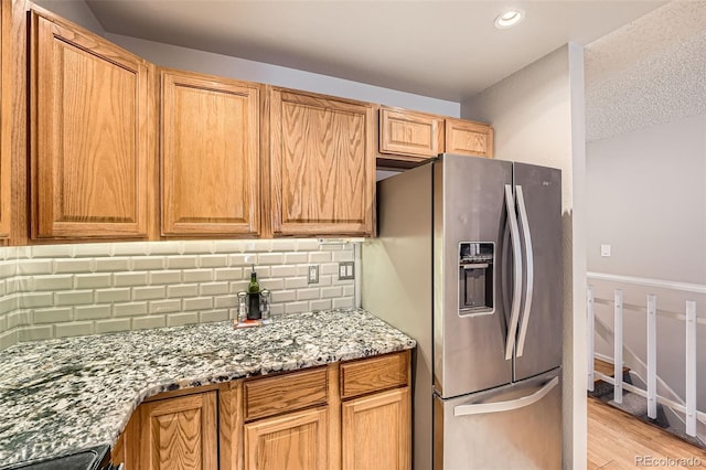 kitchen featuring light stone counters, stove, light wood-style floors, stainless steel refrigerator with ice dispenser, and decorative backsplash