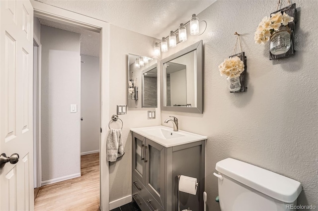 half bath featuring a textured ceiling, a textured wall, toilet, wood finished floors, and vanity