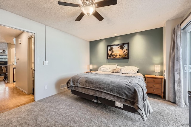 bedroom with a ceiling fan, a textured ceiling, visible vents, and light carpet