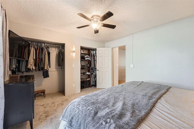bedroom with a textured ceiling, carpet, a ceiling fan, and two closets