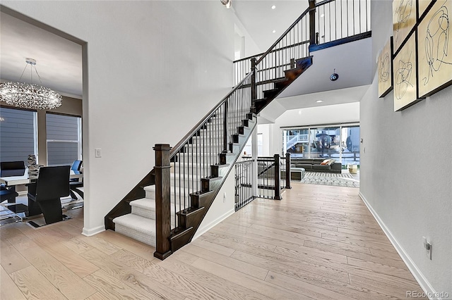 stairway featuring a towering ceiling, a notable chandelier, baseboards, and wood finished floors