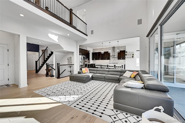 living room with light wood finished floors, visible vents, a towering ceiling, baseboards, and stairs