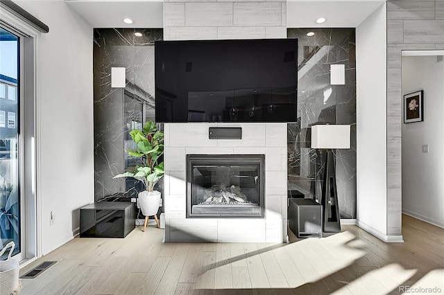 living room with baseboards, visible vents, a tiled fireplace, and wood finished floors