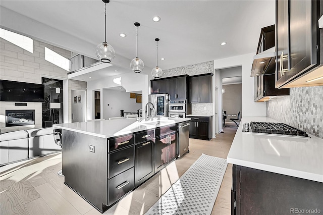 kitchen featuring decorative backsplash, appliances with stainless steel finishes, light countertops, under cabinet range hood, and a sink