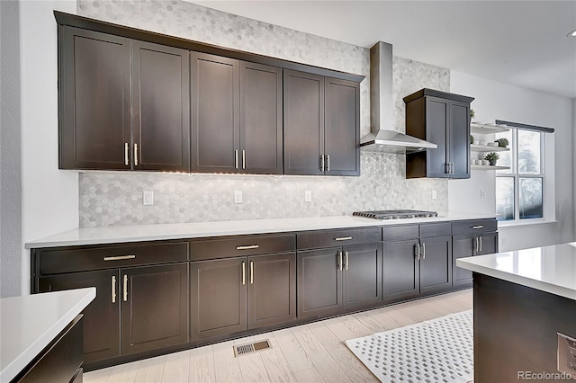 kitchen with tasteful backsplash, visible vents, light countertops, wall chimney range hood, and stainless steel gas stovetop