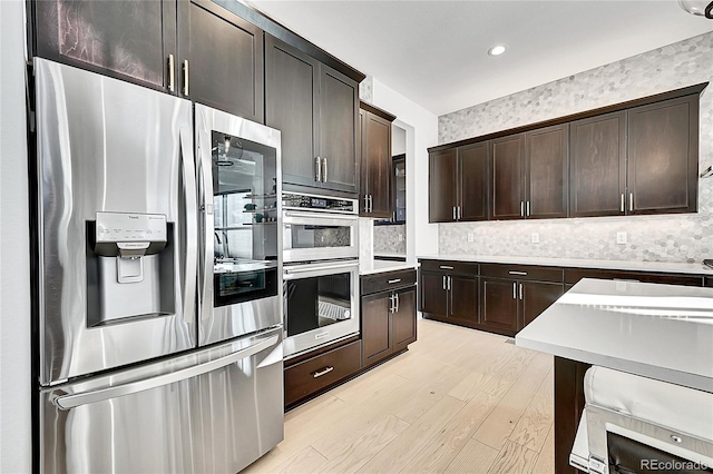 kitchen featuring stainless steel appliances, dark brown cabinets, light countertops, and light wood-style flooring