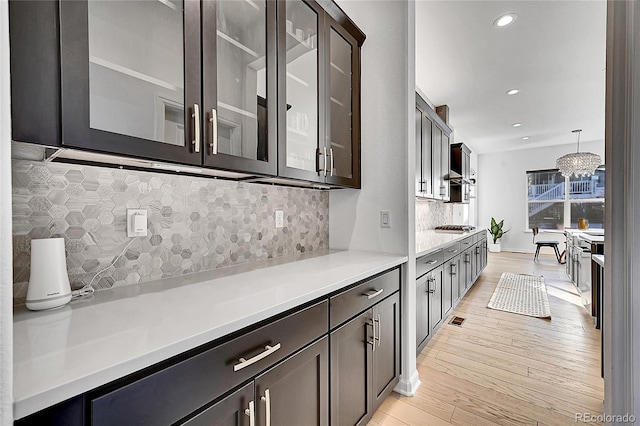 kitchen with light countertops, decorative backsplash, light wood-style floors, glass insert cabinets, and dark brown cabinetry