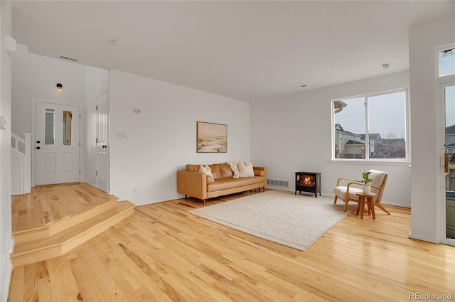 living area with a wood stove, light wood finished floors, and visible vents