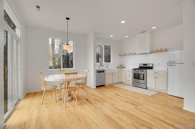 kitchen featuring light wood finished floors, visible vents, wall chimney exhaust hood, stainless steel appliances, and open shelves