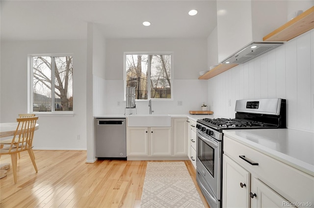 kitchen with white cabinets, stainless steel appliances, light countertops, light wood-style floors, and a sink