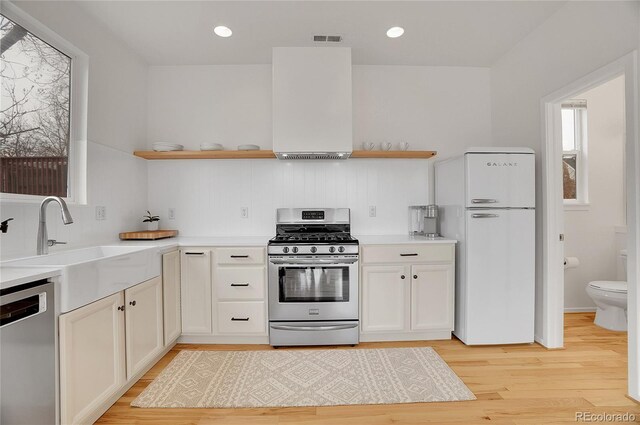 kitchen with stainless steel appliances, a sink, visible vents, open shelves, and light wood finished floors