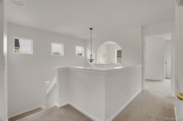 hallway with an upstairs landing, carpet, arched walkways, and baseboards