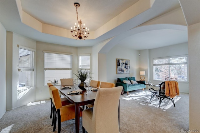 carpeted dining room featuring a tray ceiling and a notable chandelier