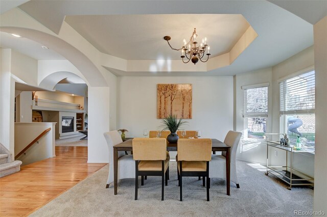 dining area with a raised ceiling, light colored carpet, and an inviting chandelier