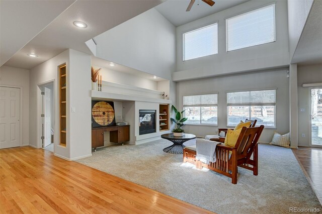 living room with built in shelves, ceiling fan, light carpet, and a high ceiling